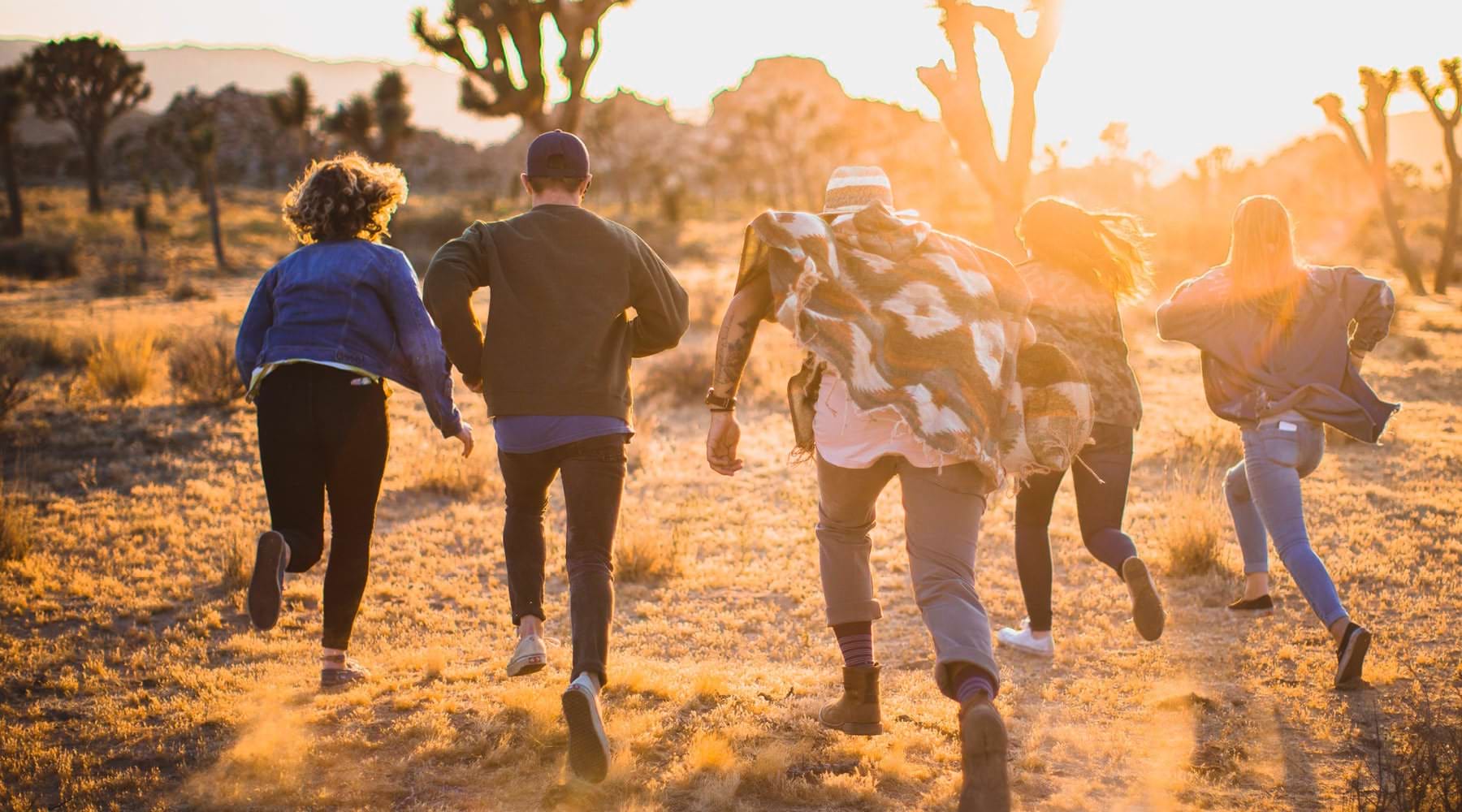 Bask in a new type of living. young adults run through the desert toward the setting sun